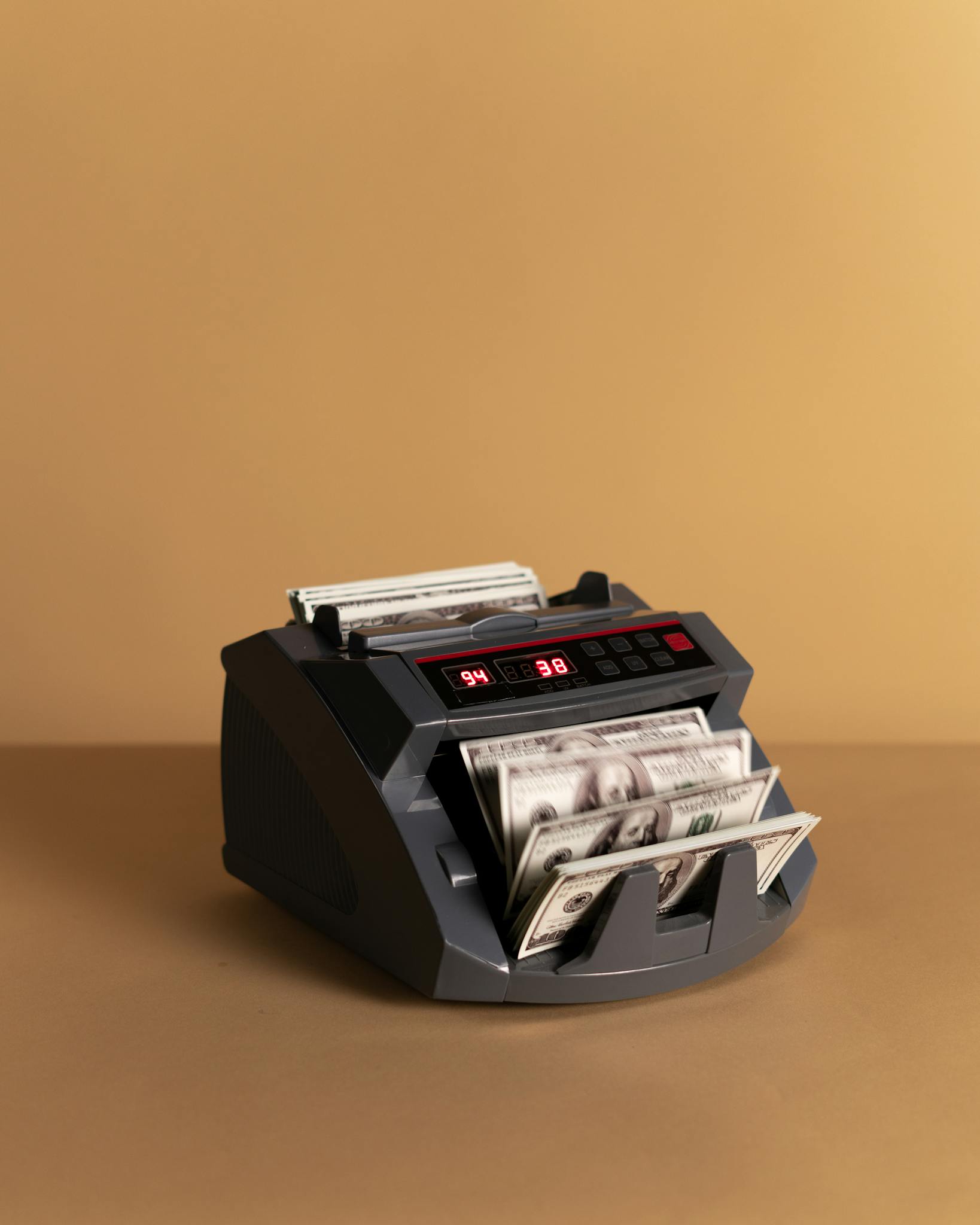 Electronic money counter processing US dollars on a neutral background.